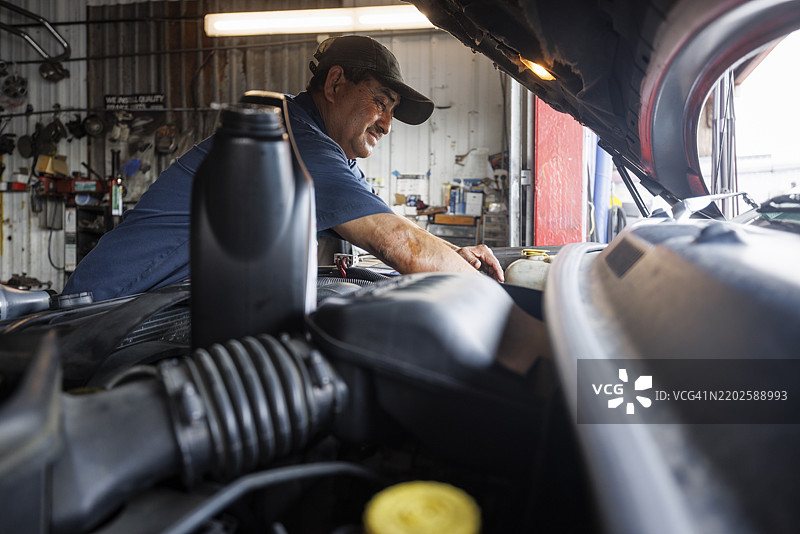 更换机油。中年西班牙裔机械师检查车辆的发动机部件。图片素材