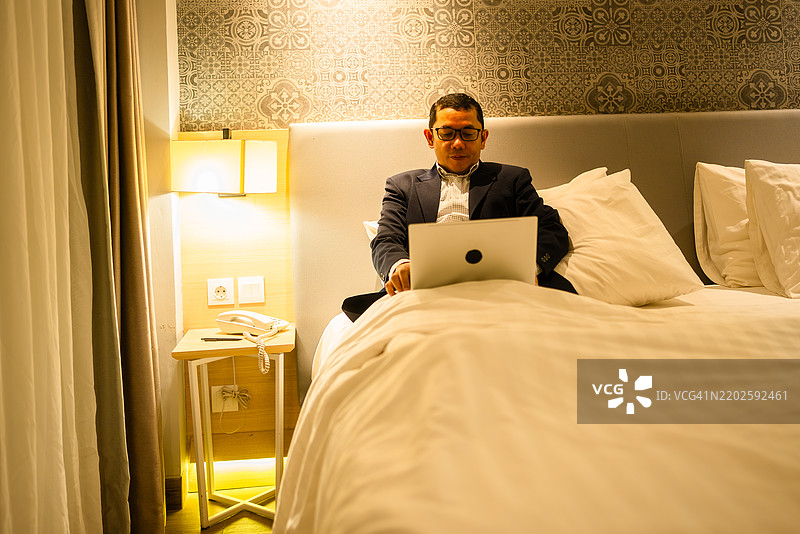 商人在酒店房间的床上使用笔记本电脑图片素材