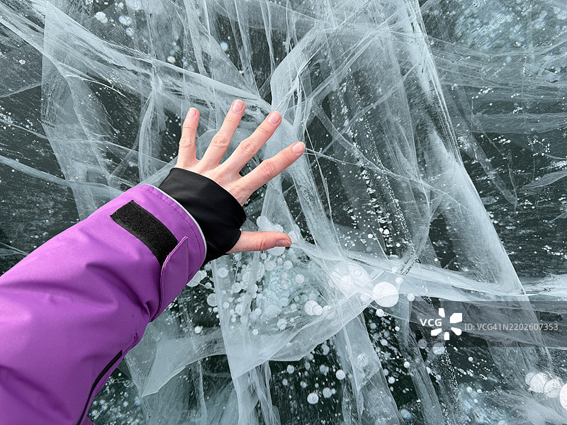 女人的手触摸着冰冻的贝加尔湖表面，湖中有甲烷气泡。图片素材