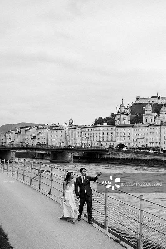 一对年轻情侣在正午时分沿着河边的步道漫步。图片素材