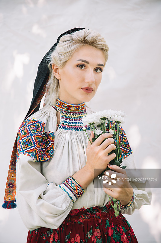 年轻女性身穿传统服饰，在白色背景前于白天摆姿势。图片素材