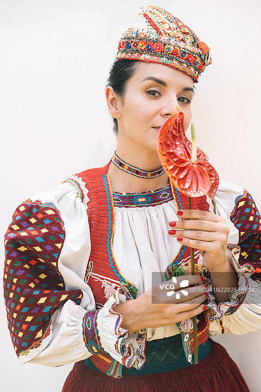 一位女性展示着色彩鲜艳的传统服装，同时调皮地用一朵鲜红的花朵遮住她的脸。图片素材