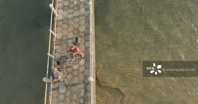 日出时分，情侣在码头上骑自行车的鸟瞰图图片素材