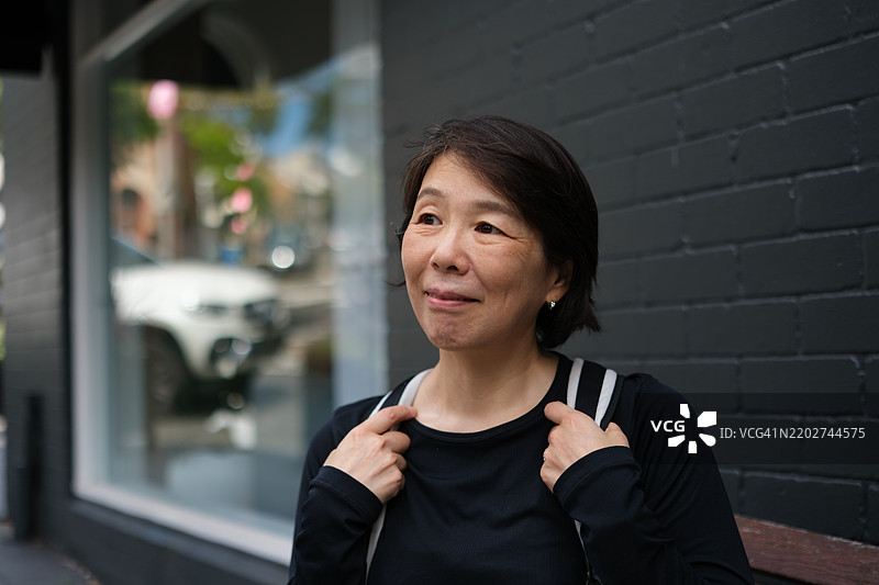 微笑的日本女性站在黑色砖墙旁边图片素材