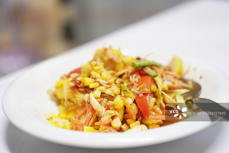 青木瓜沙拉配番茄、辣椒和大蒜，加入虾仁，搭配桌上的蔬菜，泰国菜，味道酸甜辣咸。图片素材