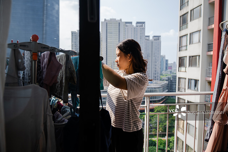 微笑的年轻女性在阳台上晾衣服图片素材