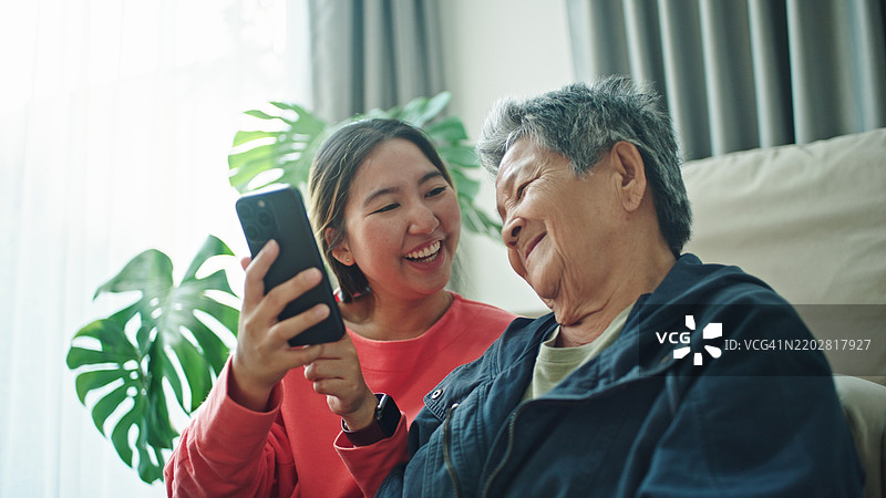 老年人与孙女一起放松地看智能手机。图片素材
