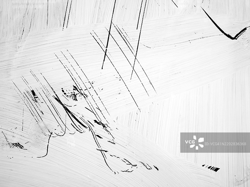 明亮的白色油漆刮痕留在墙上。粗糙的纹理。阳光。黑白色调。图片素材