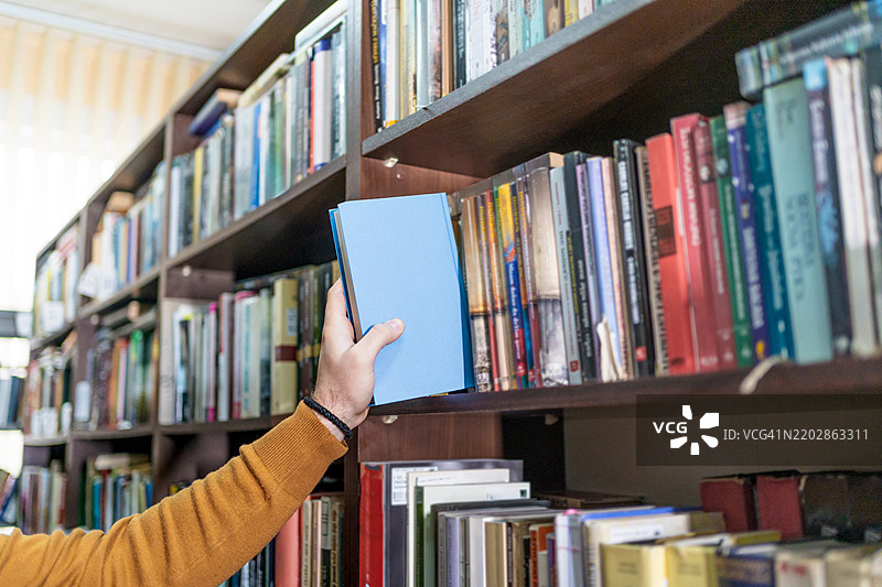 男人的手从图书馆书架上拿一本书图片素材