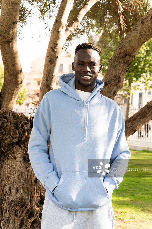 年轻男子穿着蓝色连帽衫在公园里摆姿势图片素材