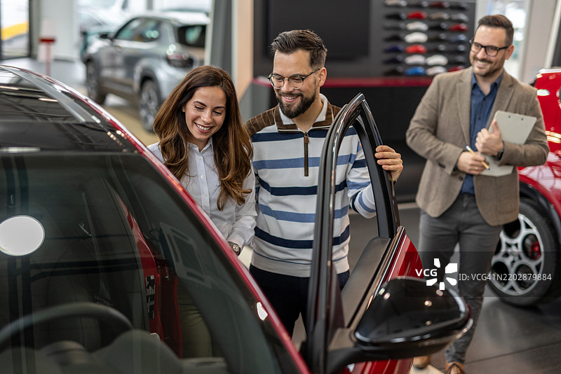 一对情侣在汽车经销商处与销售人员一起查看新车图片素材