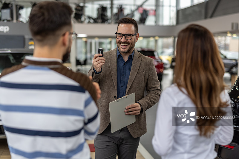 快乐的汽车销售员在经销商处将钥匙递给一对夫妇图片素材