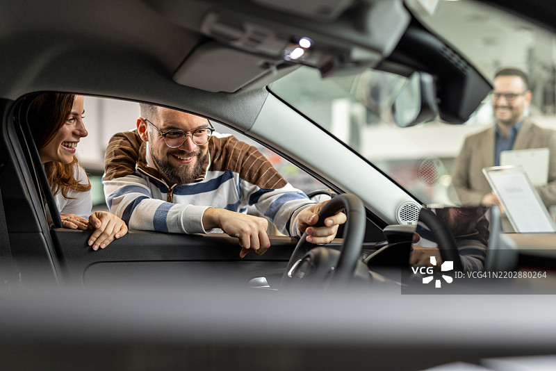 快乐的情侣在汽车经销商处与销售员一起查看新车图片素材