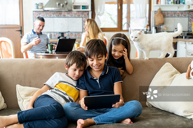 孩子们在看平板电脑，背景中有父母。图片素材
