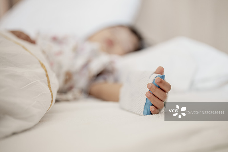 聚焦可爱的亚洲小女孩在医院接受护理，手中插着静脉输液：儿科康复场景图片素材