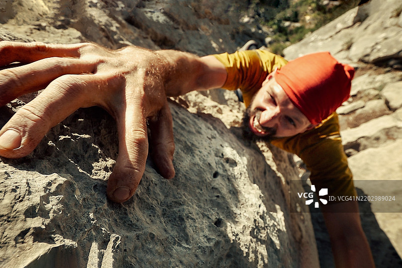 攀岩者在攀登过程中紧握悬崖 - 戴着红色头巾的男子在攀爬岩石山时面露决心的痛苦表情图片素材