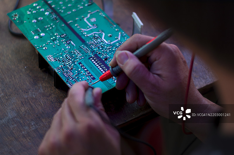 戴着蓝色手套的手握着印刷电路板芯片组件，背景是印刷电路板的生产过程。图片素材