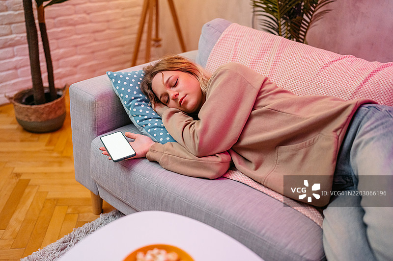 年轻女性在沙发上夜间使用手机时入睡图片素材