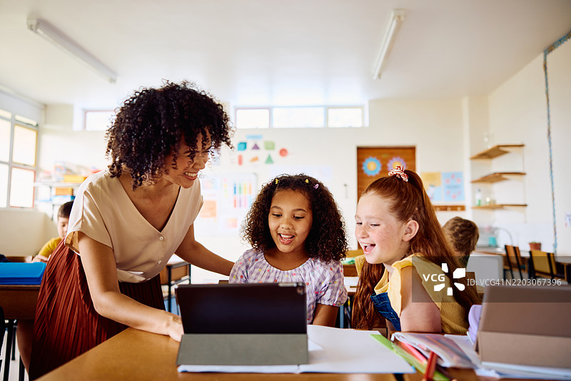 快乐的年轻女教师正在用数字平板电脑向女学生讲解，笑得很开心图片素材