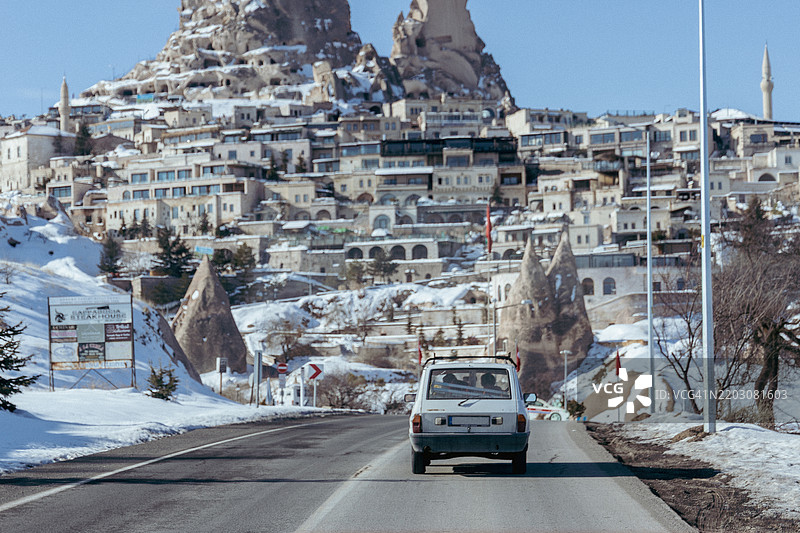 复古汽车沿着通往鸽子谷的道路行驶，背景是被雪覆盖的乌奇希萨尔城堡，中央安纳托利亚，土耳其图片素材
