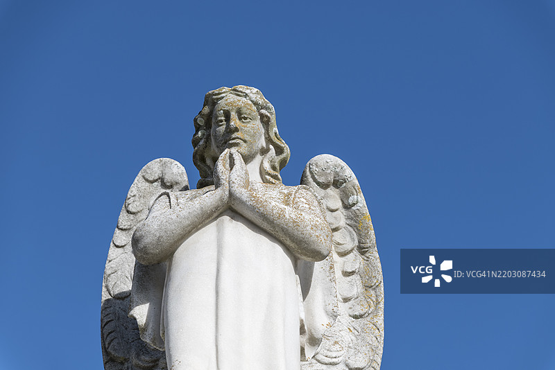 祈祷双手的天使雕像与晴朗的天空图片素材