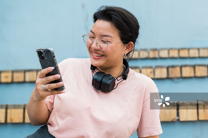 一名韩国女学生坐在公园里，正在用智能手机浏览社交网络。图片素材