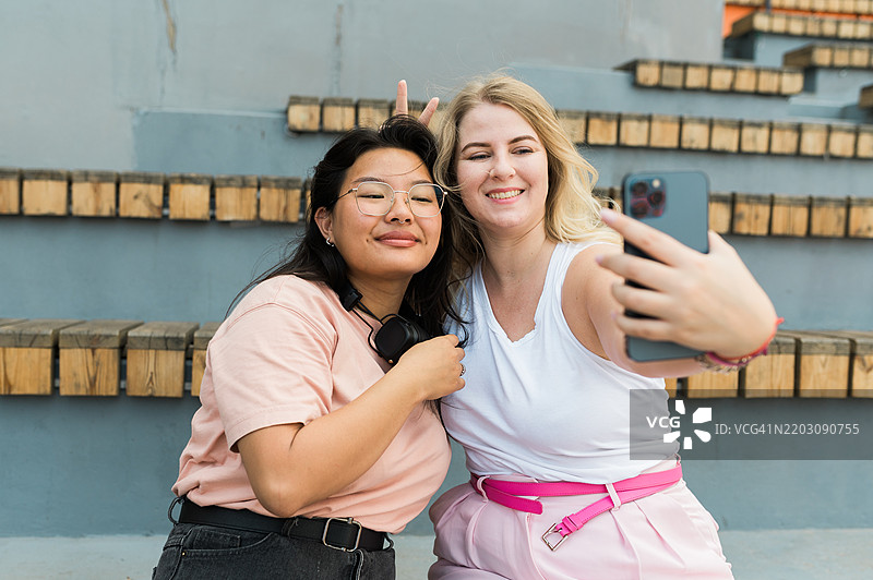 两位年轻女性博主在智能手机上自拍。女性友谊图片素材