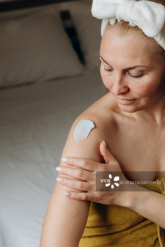 一位女性正在将抗衰老面霜涂抹在皮肤上，日常护肤和身体护理。金色涂抹的面霜或乳液在皮肤上的质地。图片素材