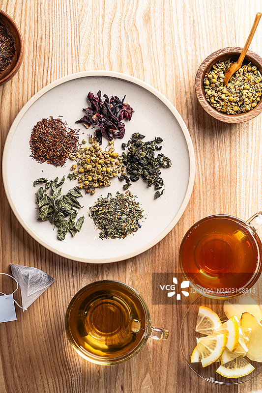 各种草药茶叶放在盘子里，草药茶在玻璃杯中。图片素材