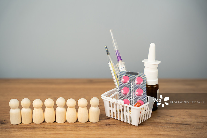 一排人形玩偶站在购物篮旁，篮子里装着药品，体现儿童、老年人和人群免疫接种的疫苗接种概念，关注健康与福祉。图片素材