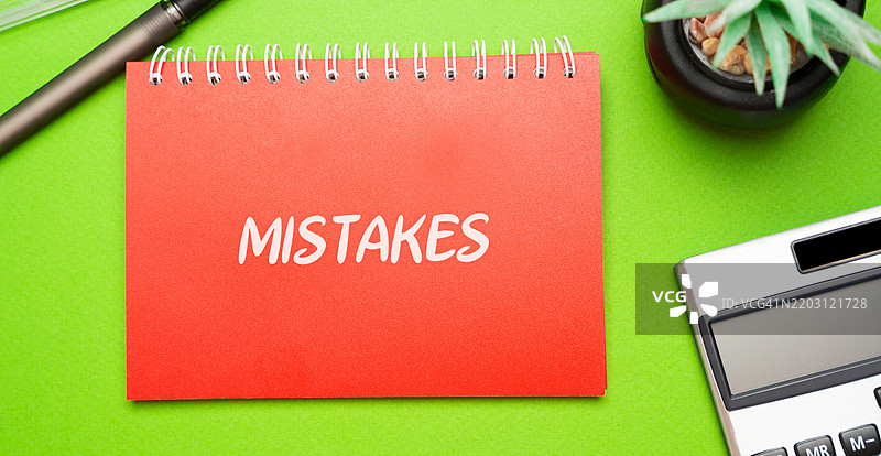 桌子上的笔记本，上面写着“错误、失误、疏忽或在经营管理业务过程中做出的不良决策”，旁边有计算器和花朵，俯视图。图片素材