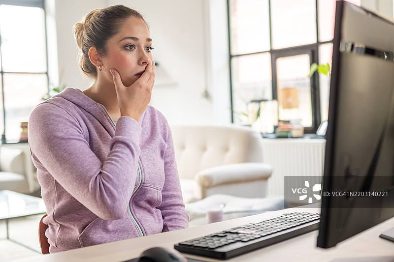 担忧的女性在家办公环境中注视电脑屏幕图片素材