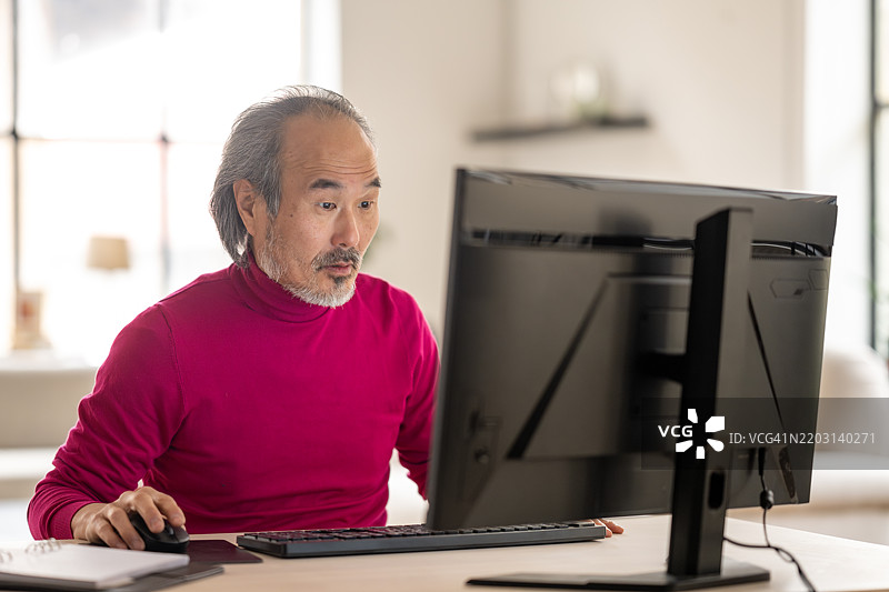 困惑的成熟亚洲男子在家中办公室使用桌面电脑图片素材