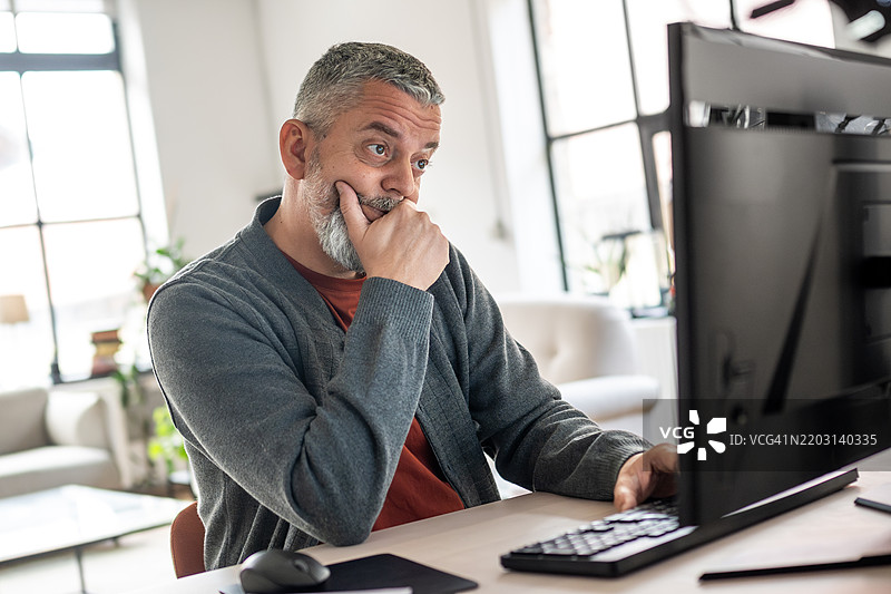 关心的成熟白人男性在桌面电脑上工作图片素材