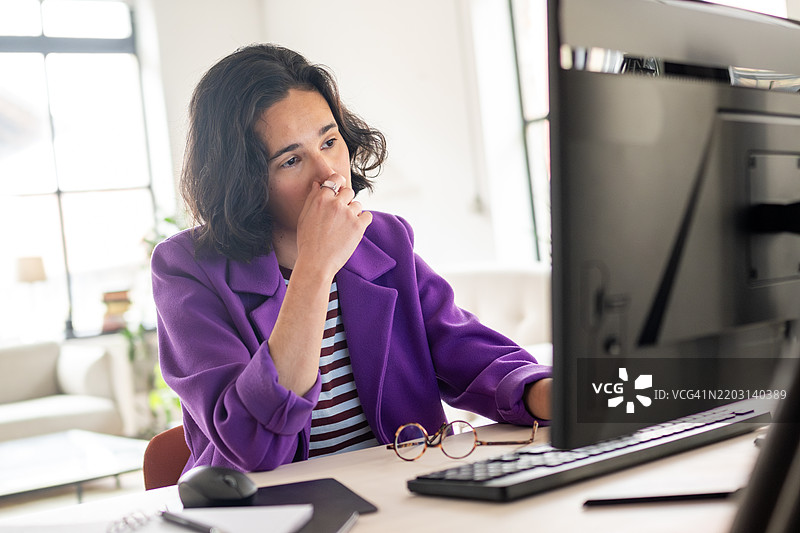在家中使用台式电脑工作的深思熟虑的西班牙裔女性图片素材
