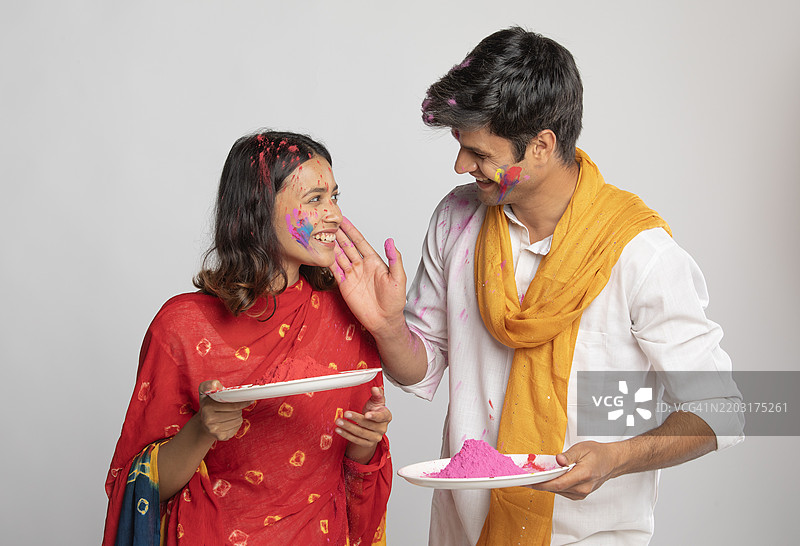 年轻情侣在白色背景下用彩色面粉玩霍利节图片素材