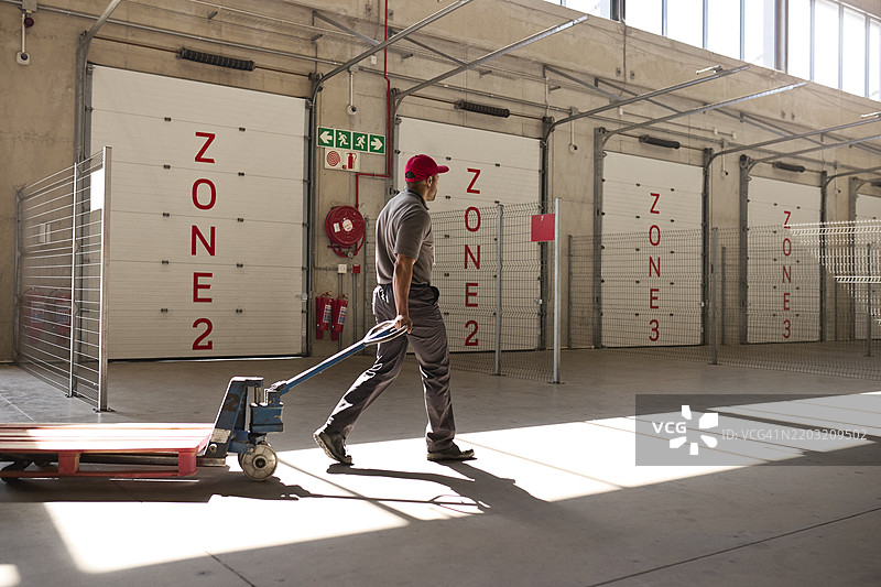 男性仓库工人推着空手推车走动图片素材