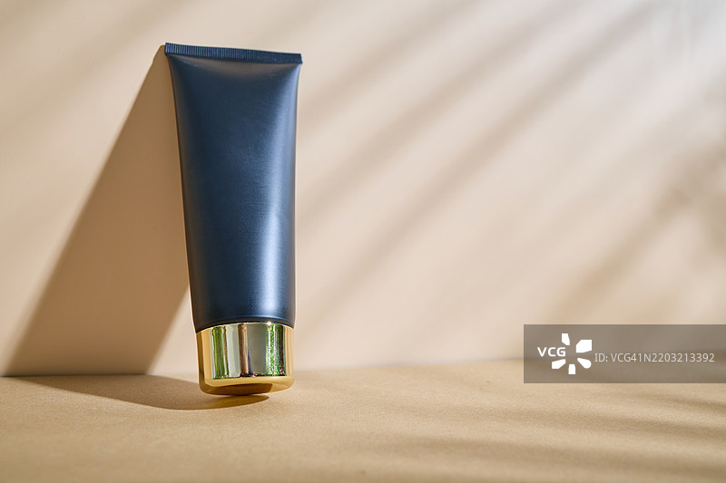 黑色奶油管放在米色背景上，旁边有棕榈叶的阴影。产品展示概念图片素材