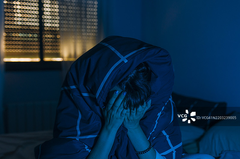晚上坐在床上的抑郁女性用双手遮住脸部图片素材