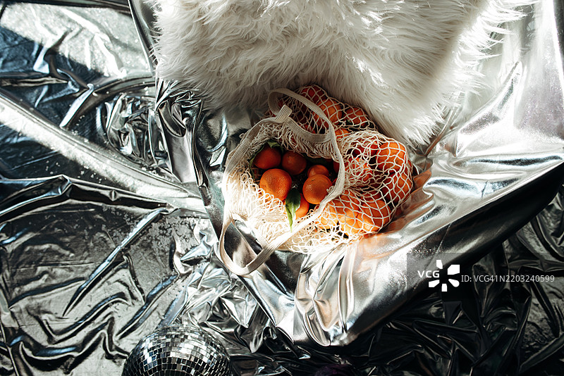 银色背景上的绳网袋装橘子。现代风格。迪斯科风格。现代时尚静物。图片素材