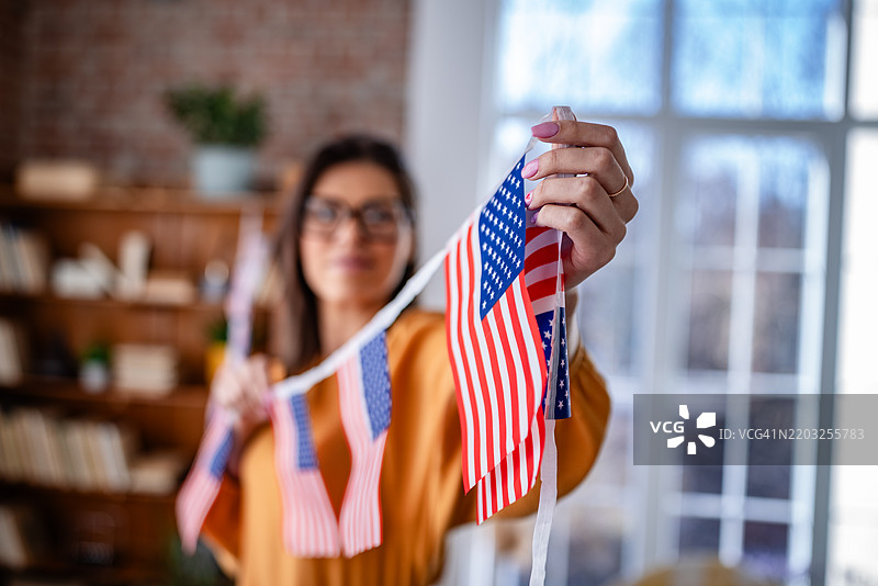 年轻女性愉快地装饰她温馨的家，用五彩缤纷的旗帜庆祝节日，脸上洋溢着快乐的笑容。图片素材