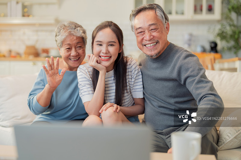 亚洲家庭的温馨时刻，年轻女性与父母在客厅中进行生动的视频通话，捕捉到与远方家人交流的快乐与团聚的瞬间，传递爱与亲情的美好氛围。图片素材