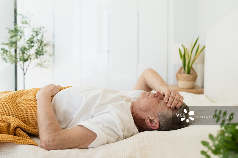 疲惫的老年男子躺在床上，捂着头醒来图片素材