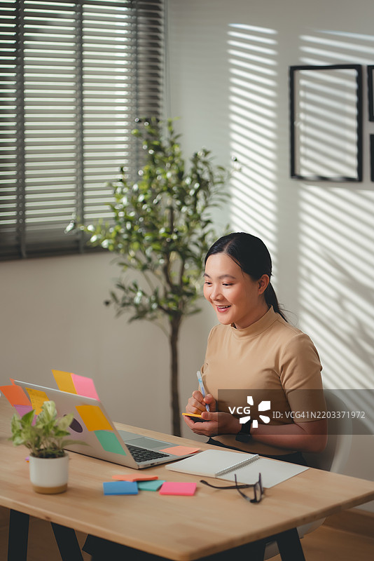 亚洲女性在家办公室愉快地工作并做笔记。图片素材