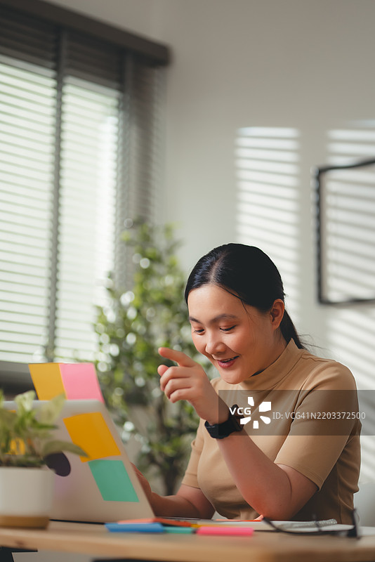 亚洲女性在家办公室愉快地使用笔记本电脑工作。图片素材