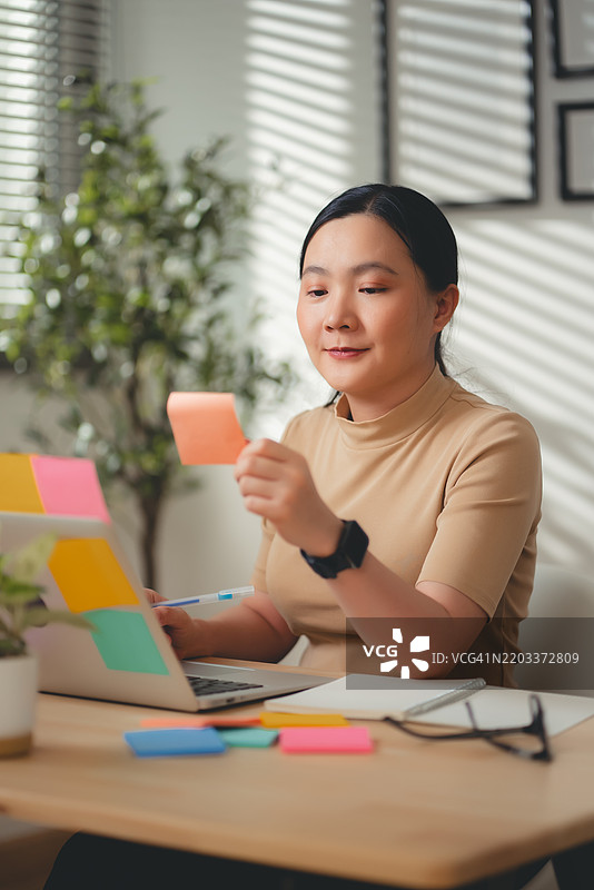 亚洲女性在家办公室愉快地工作并做笔记。图片素材