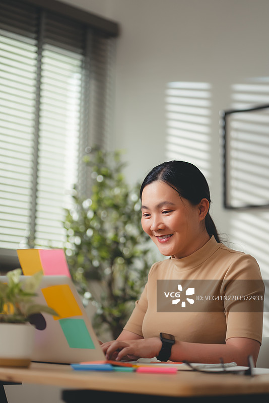 亚洲女性在家办公室享受在线工作，坐在椅子上打字。图片素材