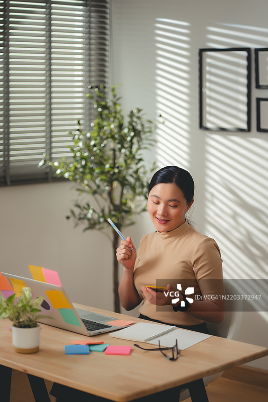 亚洲女性在家办公室愉快地工作并做笔记。图片素材
