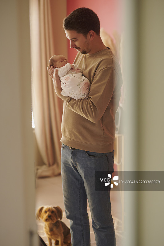 父亲、狗和抱着熟睡婴儿在家中，促进成长发展，与婴儿拥抱以建立联系。敞开的门，爱的父亲在儿童成长中提供支持，婴儿小憩，关爱与梦境相拥。图片素材