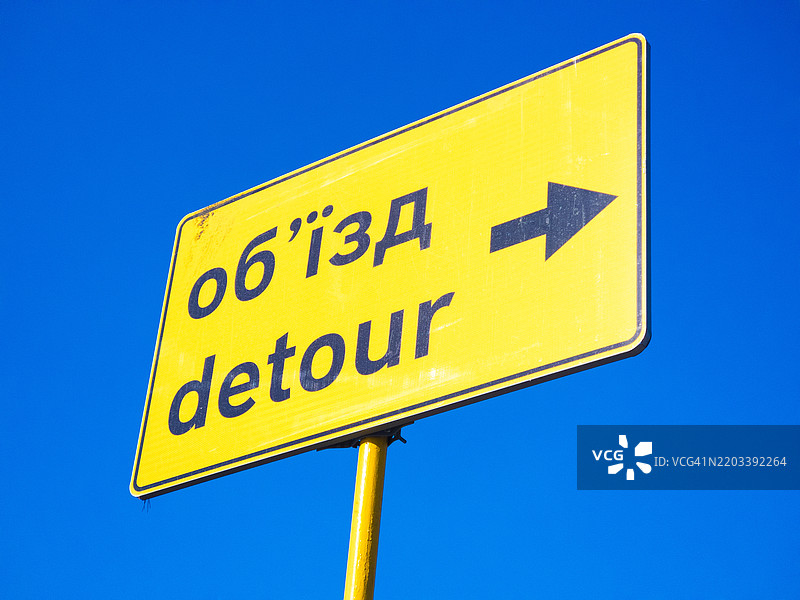 在清澈的蓝天背景下，指示车辆在繁忙区域改变行驶路线的方向性绕行标志图片素材